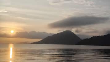 Une étendue d’eau calme où se reflète le soleil, avec une montagne en arrière-plan et un ciel nuageux.