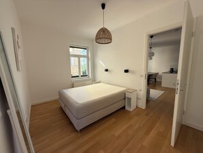 A bedroom with a single bed, a bedside table, a window, and a door leading to a bathroom. - Modern, Fully Furnished City Apartment - 5 minutes from downtown (München)