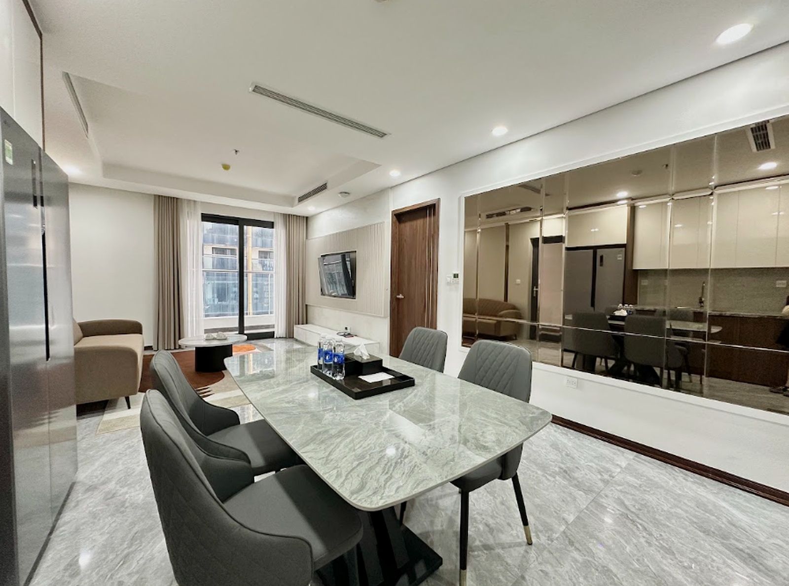 A modern hotel room with a marble dining table, comfortable seating, a television, and a view of the cityscape.