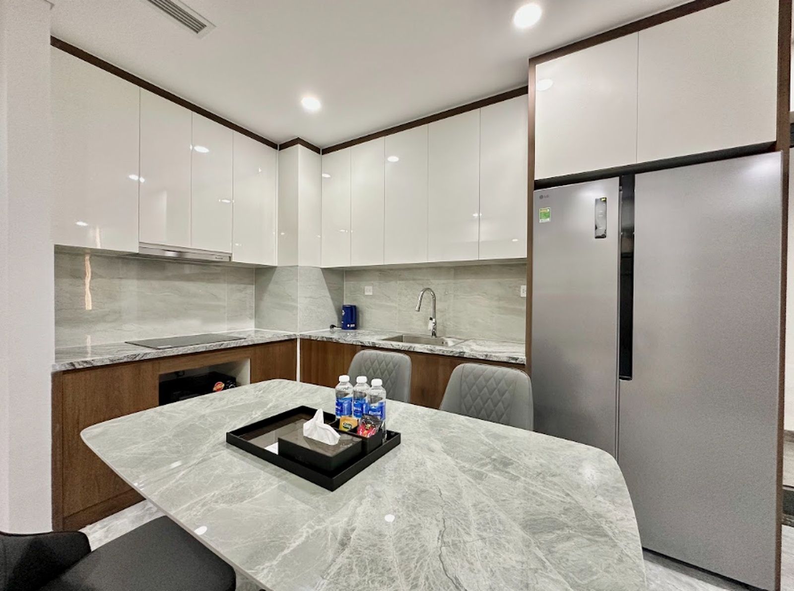 A modern kitchen with white cabinets, a marble countertop, and a stainless steel refrigerator.