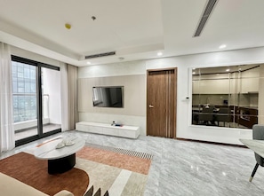 Una sala moderna con un televisor de pantalla plana montado en la pared, un sofá, una mesa de centro y un comedor con sillas.