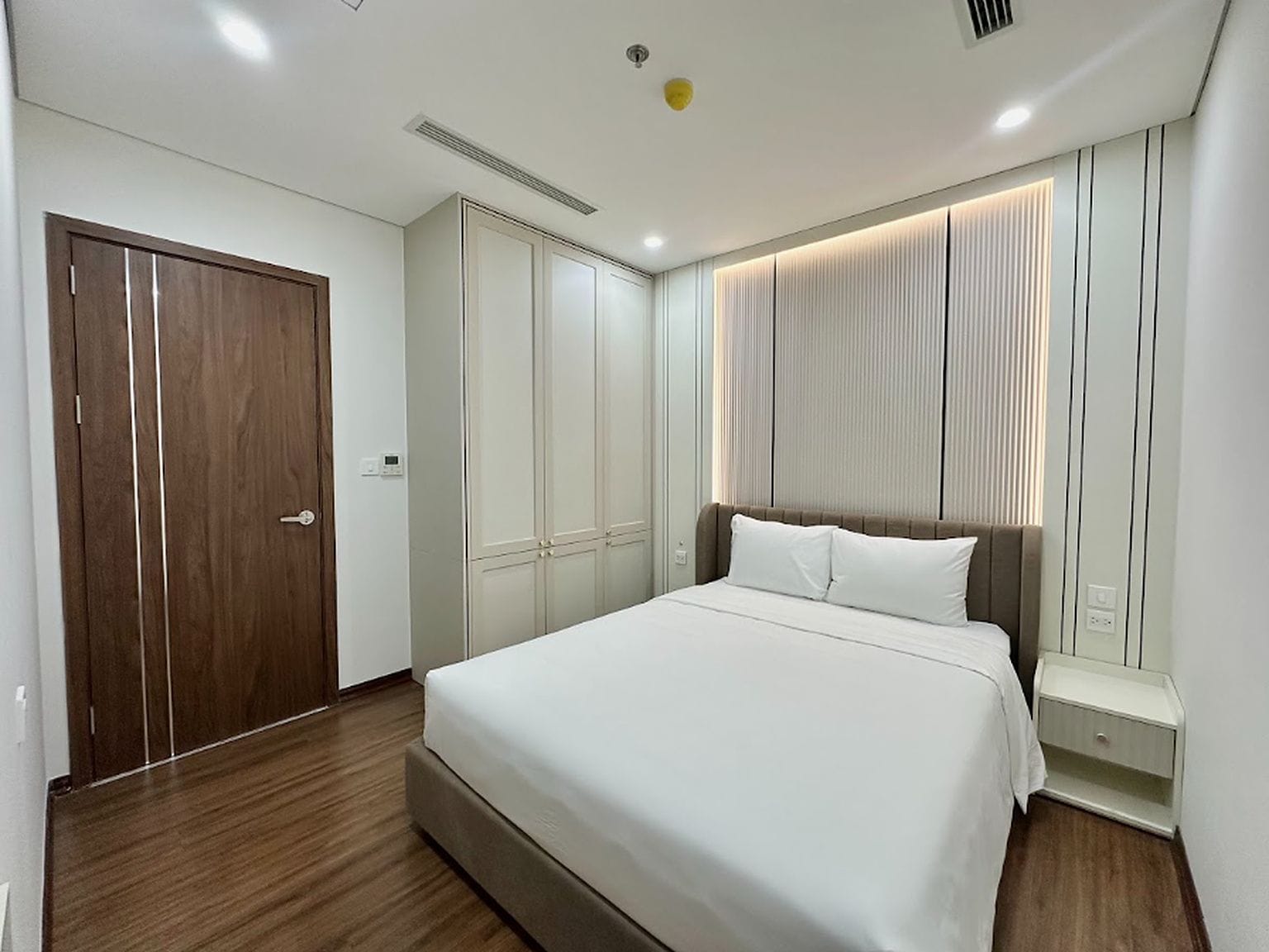 A hotel room with a large bed, a wardrobe, and a window with blinds.