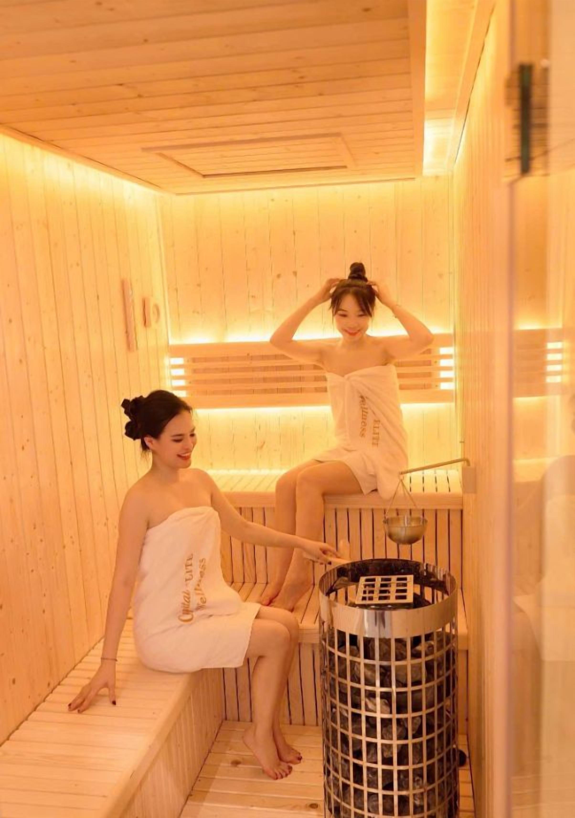 Una sauna con paredes y bancos de madera, un cubo de metal y una persona sentada en un banco.