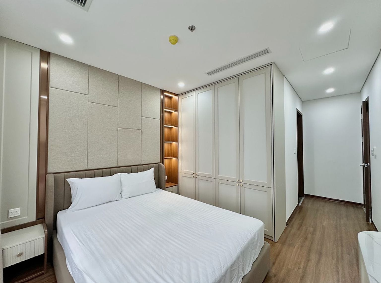 A hotel room with a large bed, built-in wardrobe, and a wooden floor.