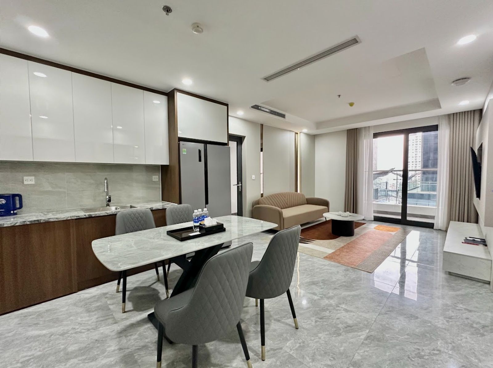 A modern hotel room with a dining area, a sofa, and a large window with a city view.