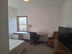 A bedroom with a single bed, a desk with a chair, a television, and a window with blinds. - Perfect 5-bedroom house with AC in charming Iowa City (Iowa City)