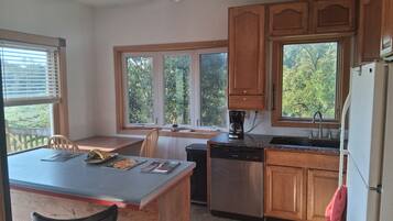A kitchen with wooden cabinets, a dishwasher, a coffee maker, and a window overlooking greenery.