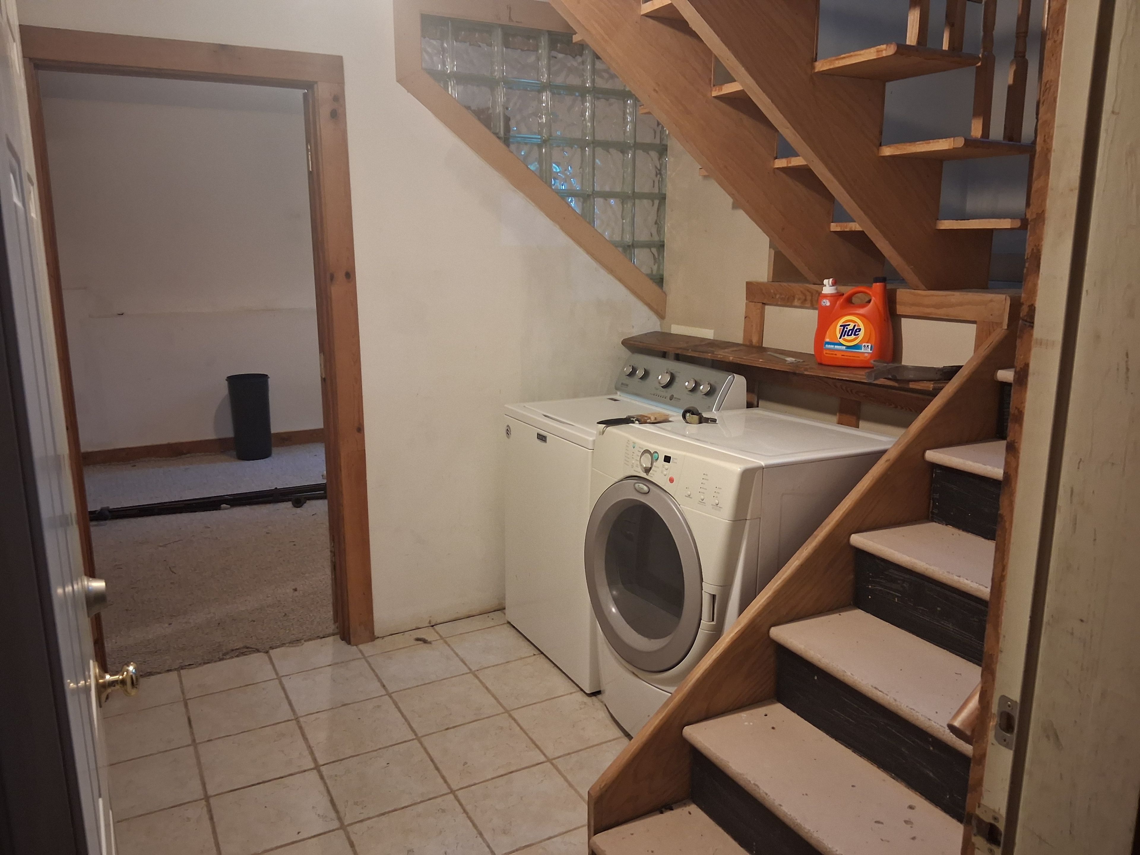 A laundry area with a washing machine, a wooden staircase, and a window with a view.