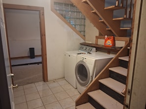 A laundry area with a washing machine, a wooden staircase, and a window with a view.