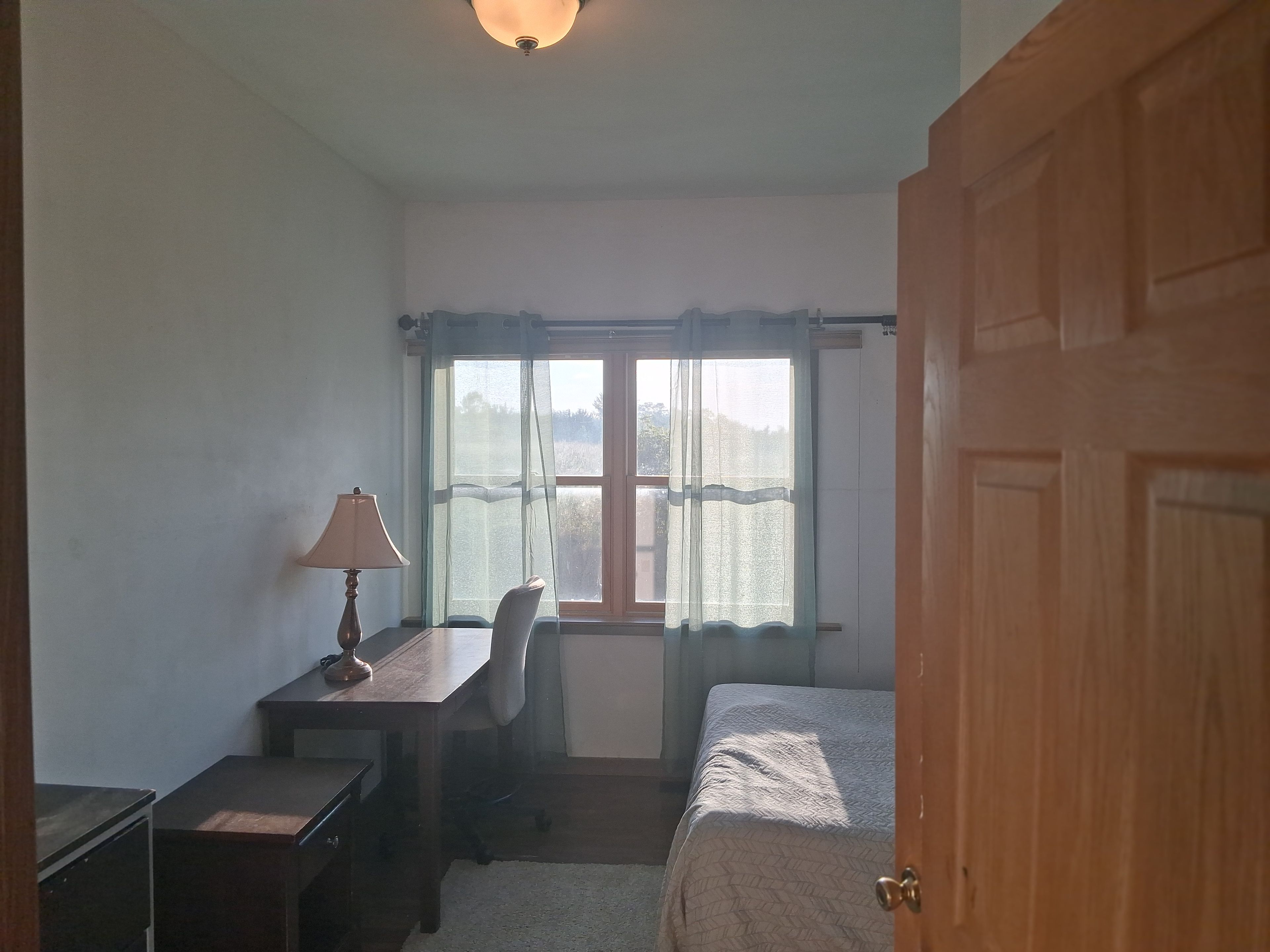 A bedroom with a bed, a desk, a chair, and a window with curtains.