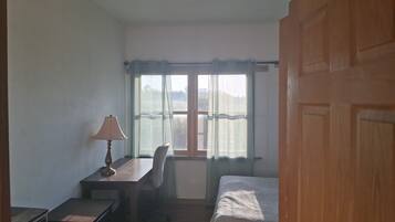 A bedroom with a bed, a desk, a chair, and a window with curtains.