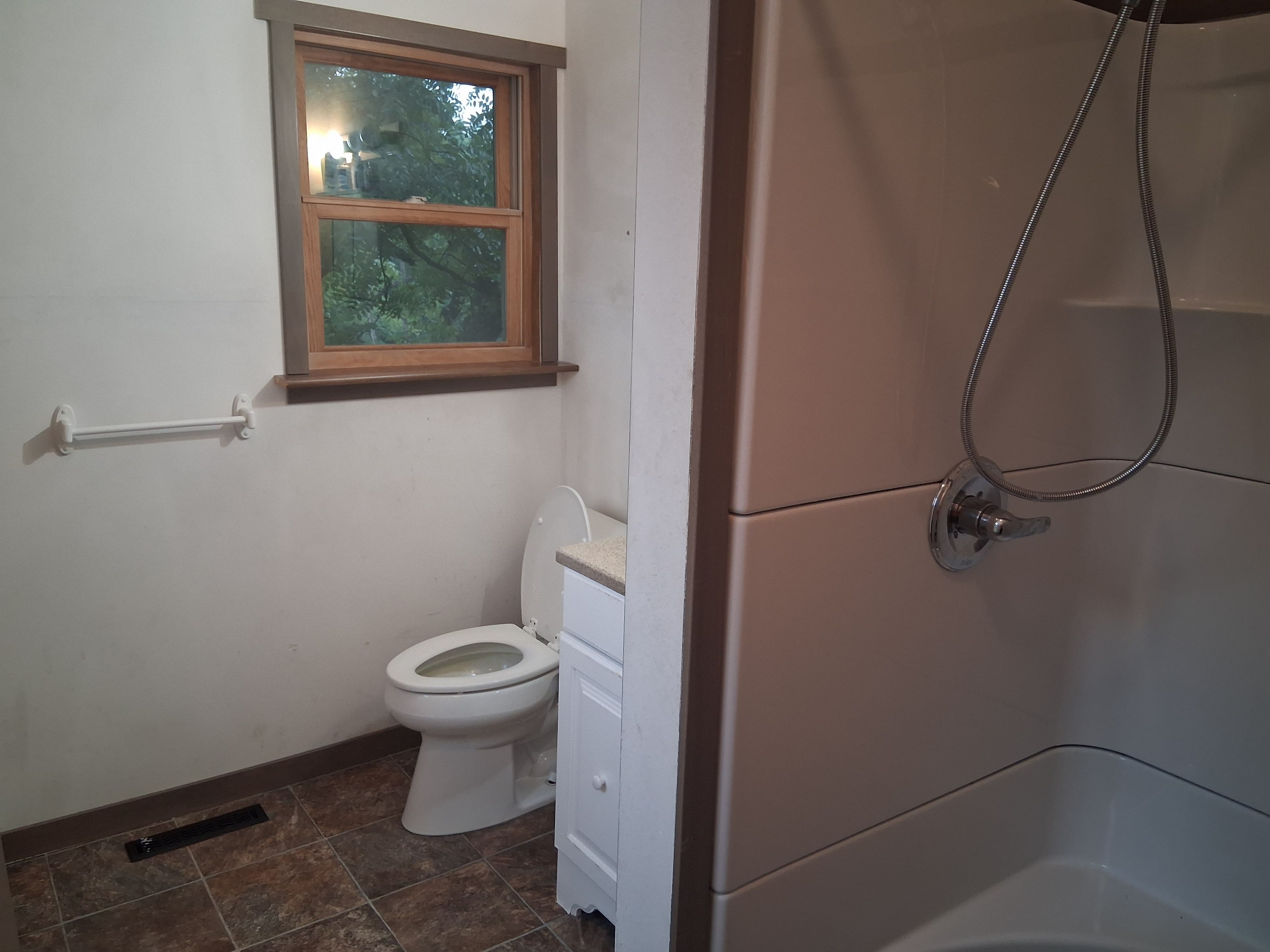 A bathroom with a toilet, a window, and a shower.