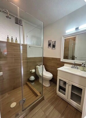 Une salle de bain moderne avec une douche à parois de verre, des toilettes et un lavabo avec un miroir au-dessus.