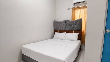 A hotel room with a bed, a wooden headboard, a window with curtains, and an air conditioning unit.