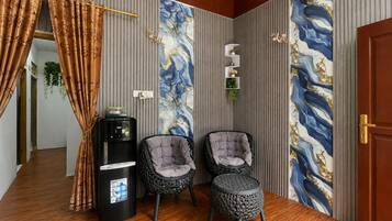 Ein Zimmer mit Wasserspender, zwei gepolsterten Sesseln, einem kleinen Hocker und einer Tür mit dekorativer Verkleidung.