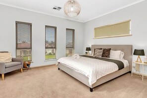 A bedroom with a large bed, two bedside tables, a chair, and a window with blinds. - Ochre Point Beach House, Moana-Seafront (Moana)