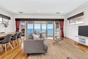 A modern living room with a sofa, dining table, chairs, and a TV. - Ochre Point Beach House, Moana-Seafront (Moana)