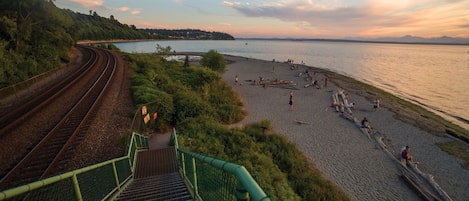 A coastal area with a railway track, a beach with people, and a forested hill.