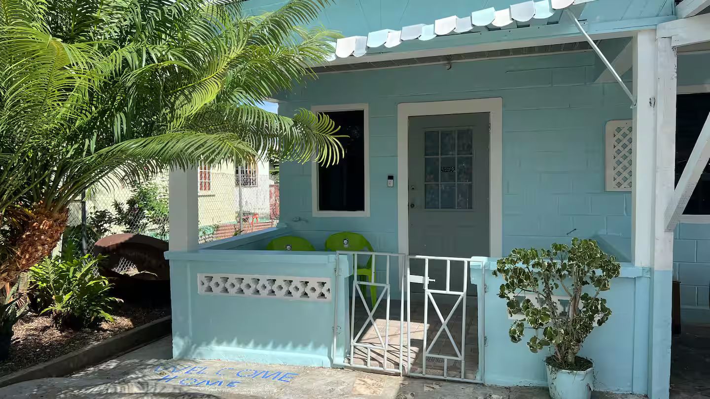 A light blue building with a gated entrance, a small porch, and a potted plant.