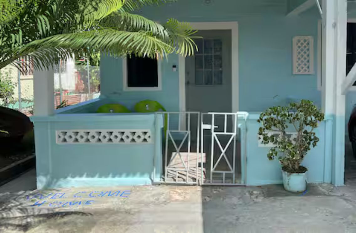 A light blue building with a gated entrance, a small window, and a potted plant.