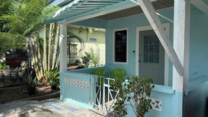 A small, light blue building with a covered porch, two green chairs, and a potted plant.