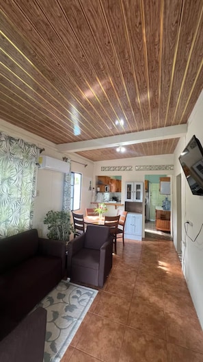 A living room with a wooden ceiling, a sofa, a coffee table, and a dining area with chairs and a table. - Caribbean Cozy Cottage in Plymouth Village (Plymouth)