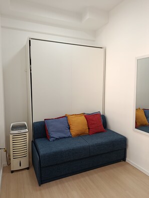 A room with a blue sofa, a white partition, and a portable heater. - New Studio República Copan- Mackenzie (São Paulo)