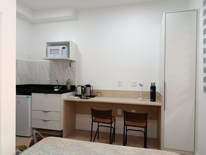 A compact room with a kitchenette, a bed, and two chairs. - New Studio República Copan- Mackenzie (São Paulo)