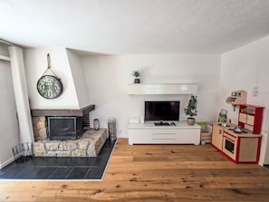 A living room with a stone fireplace, a flat-screen TV, a white entertainment unit, and a red children's play kitchen.
