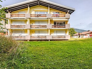 Ein mehrstöckiges Gebäude mit Balkonen, einer flachen Dachterrasse und einem Rasen im Vordergrund.