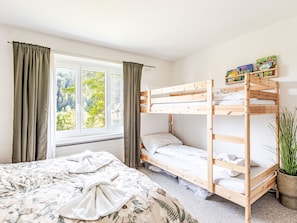 A bunk bed room with a window, curtains, a bed with a floral bedspread, and a potted plant. - Familienwohnung bei Lenzerheide by Interhome (Churwalden)