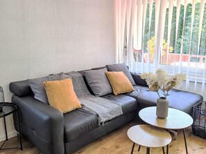 Ein modernes Wohnzimmer mit einem schwarzen Ledersofa, einer grauen Tagesdecke und einer Vase mit Blumen auf einem runden Tisch.
