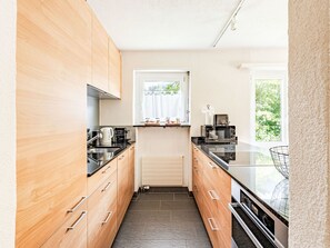 A modern kitchen with wooden cabinets, a black countertop, and a window with a view of greenery. - Familienwohnung bei Lenzerheide by Interhome (Churwalden)