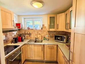 A kitchen with wooden cabinets, a sink, a stove, and a microwave. - Chalet Bärgheimet by Interhome (Saas-Fee)