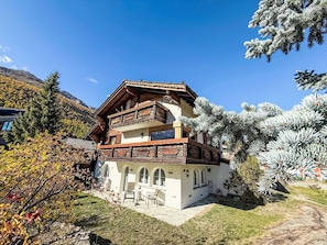 A two-story chalet with a wooden balcony, surrounded by trees and a mountain backdrop. - Chalet Bärgheimet by Interhome (Saas-Fee)
