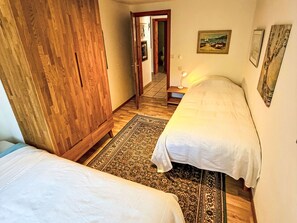 A bedroom with two beds, a wooden wardrobe, a patterned rug, and a painting on the wall. - Chalet Bärgheimet by Interhome (Saas-Fee)
