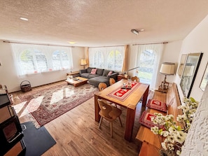 A spacious living area with a sofa, a dining table with chairs, and a large window with curtains. - Chalet Bärgheimet by Interhome (Saas-Fee)