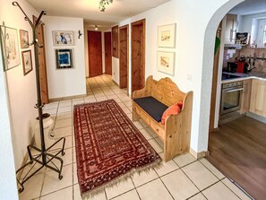 Uma sala aconchegante com um banco de madeira, um tapete estampado e uma área de jantar, com cozinha visível ao fundo.