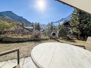 A patio with a stone table, a stone wall, and a view of mountains and a house in the background. - Chalet Bärgheimet by Interhome (Saas-Fee)
