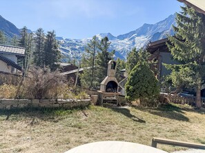 A stone fireplace surrounded by trees and a mountain view. - Chalet Bärgheimet by Interhome (Saas-Fee)