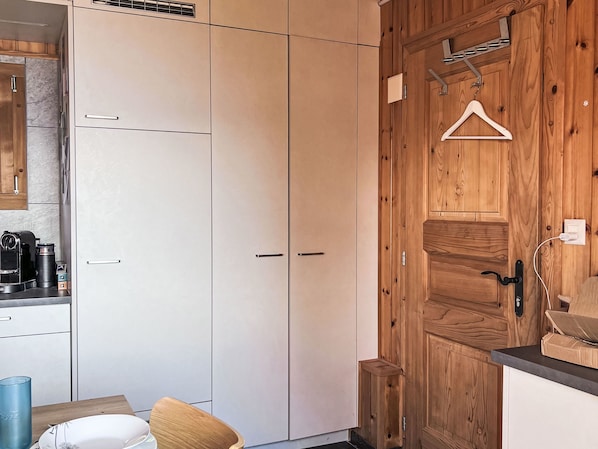 A kitchen with white cabinets, a wooden door, and a hanging coat rack.