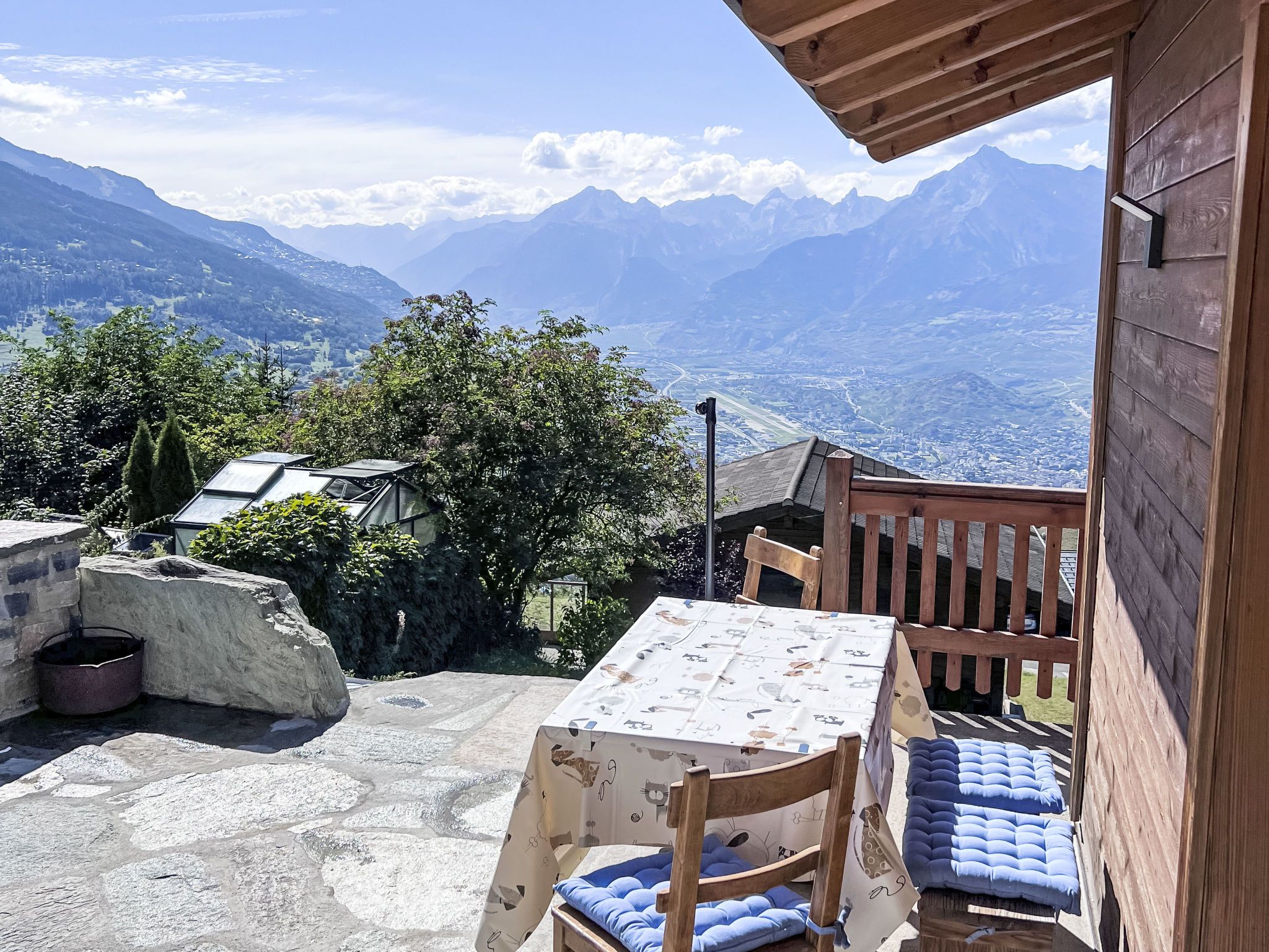 A wooden deck with a table and chairs, overlooking a mountainous landscape.