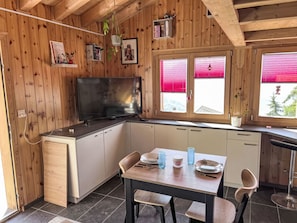 A cozy kitchen with wooden walls, a flat-screen TV, a dining table with chairs, and a window with red blinds.