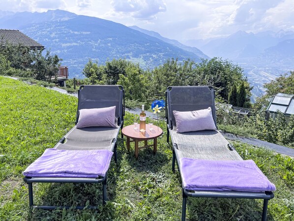 Two lounge chairs with purple cushions, a small round table with a bottle and glasses, and a scenic view of mountains in the background. - Petit chalet du leigier by Interhome (Mase)