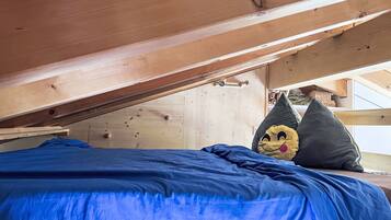 Uma cama beliche com colchão azul, vigas de madeira no teto e um urso de pelúcia no canto.