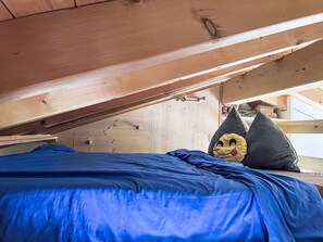 Een stapelbed met een blauwe matras, houten balken in het zicht en een teddybeer in de hoek.