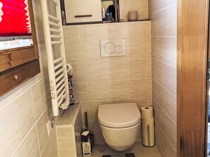 A compact bathroom with a toilet, a radiator, and a small shelf with toiletries. - Petit chalet du leigier by Interhome (Mase)