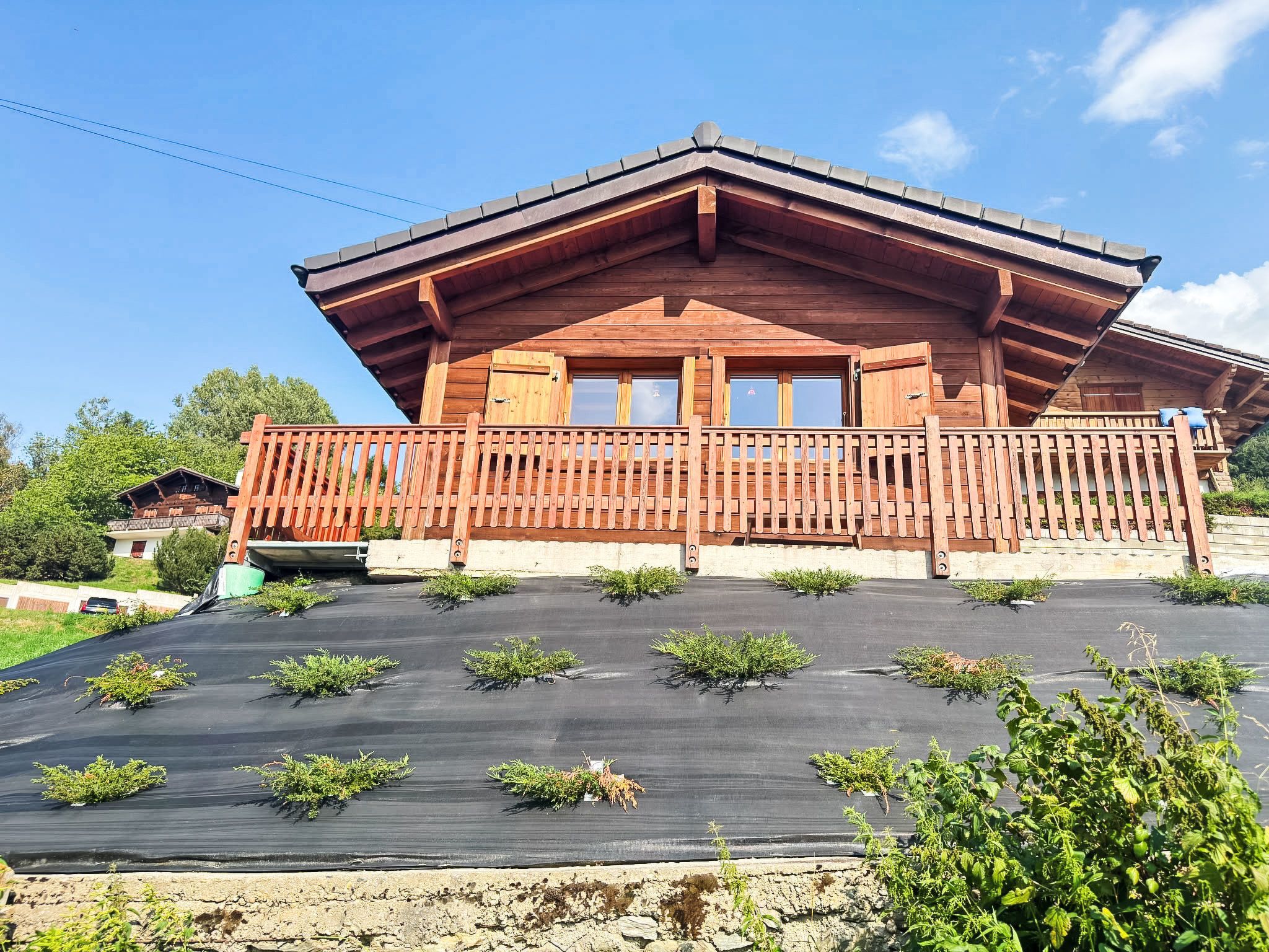 Eine Holzhütte mit Balkon, flachem Dach und einem Gartenbereich mit Pflanzen.