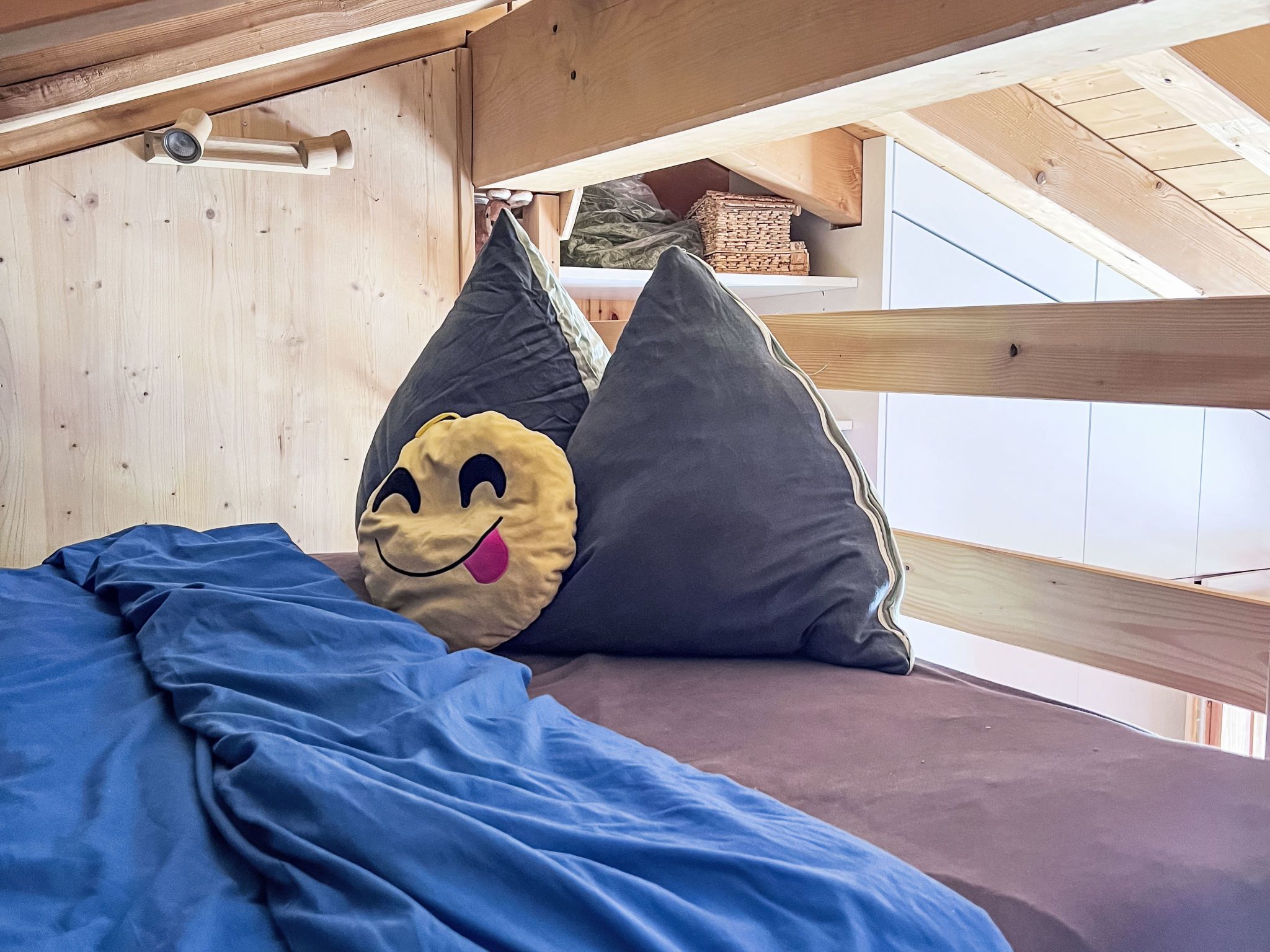 Ein Etagenbett mit einer blauen Decke und zwei Kissen, eines mit einem Smiley-Design.