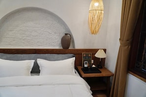 Habitación de hotel con una cama, una mesita de noche, una lámpara, un florero y una pared con textura.